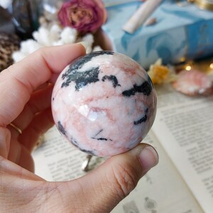 May include: A pink and black sphere made of polished stone. The sphere has a swirling pattern of pink and black.