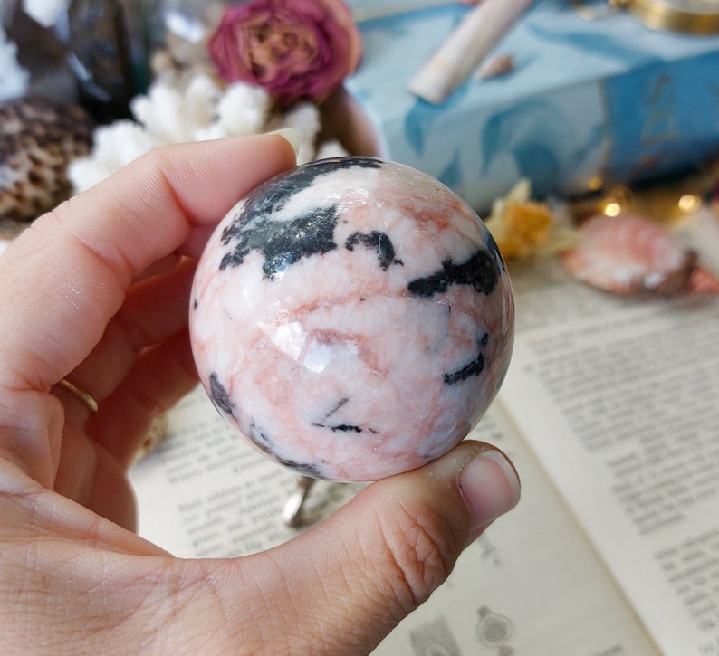 May include: A pink and black sphere made of polished stone. The sphere has a swirling pattern of pink and black.