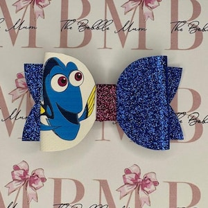 May include: A blue and white glitter bow featuring a character from the film Finding Dory. The bow is decorated with a burgundy glitter ribbon.