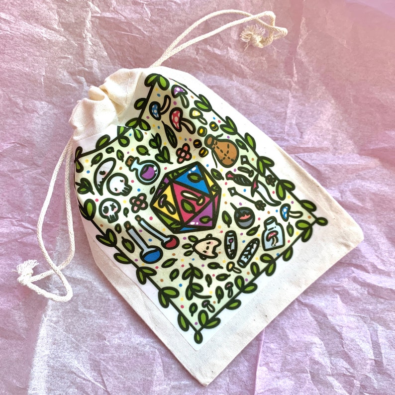 Puede incluir: Una bolsa de cord&oacute;n de color crema con un gr&aacute;fico colorido de un dado de m&uacute;ltiples caras, botellas de pociones, setas y otros elementos de fantas&iacute;a. El dise&ntilde;o est&aacute; enmarcado por vides y hojas verdes. La bolsa est&aacute; hecha de una tela suave y natural.