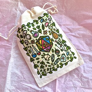 Puede incluir: Una bolsa beige con cord&oacute;n y un gr&aacute;fico colorido de un dado D20, setas, botellas de pociones y otras ilustraciones de fantas&iacute;a. El dise&ntilde;o est&aacute; enmarcado por hojas y enredaderas verdes. La bolsa est&aacute; hecha de tela natural.