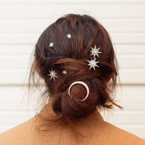 May include: A woman with brown hair wearing a brown coat has her hair styled in a bun with multiple silver star-shaped hair clips and a silver crescent moon hair clip.