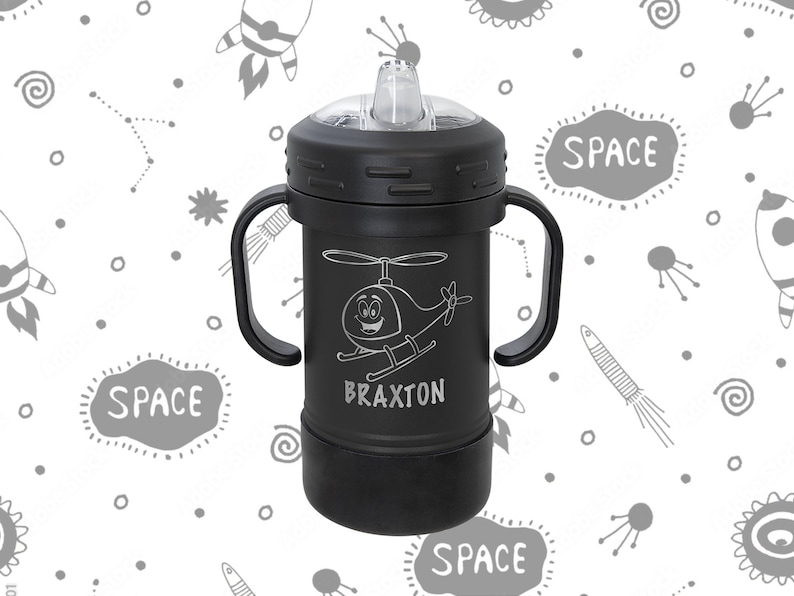 Może przedstawiać: Czarny kubek do picia z dwoma uchwytami, przezroczystą pokrywką i słomką. Kubek ma rysunek helikoptera i napis "BRAXTON" nadrukowany na nim. Tło jest białe z wzorem o tematyce kosmicznej.