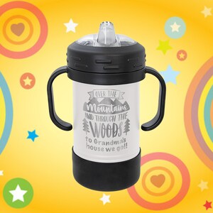 Może przedstawiać: Biały kubek ze stali nierdzewnej z czarnymi uchwytami i czarną pokrywką. Na kubku nadrukowany jest tekst "Over the Mountains and Through the Woods to Grandma's house we go!"