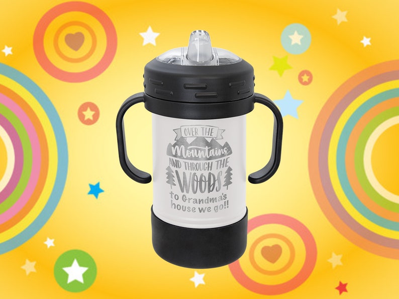 Może przedstawiać: Biały kubek ze stali nierdzewnej z czarnymi uchwytami i czarną pokrywką. Na kubku nadrukowany jest tekst "Over the Mountains and Through the Woods to Grandma's house we go!"