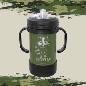 Może przedstawiać: Zielony kubek ze stali nierdzewnej z czarnymi uchwytami i czarną pokrywką. Kubek przedstawia kresk&oacute;wkowego szopa pracza i napis "Riverside Zoo".