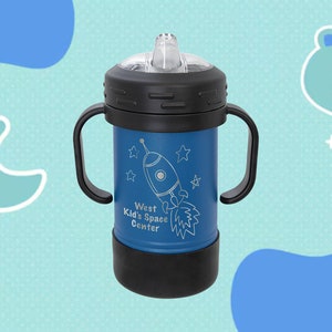Może przedstawiać: Niebieski kubek ze stali nierdzewnej z czarną pokrywką i uchwytami. Kubek ma wz&oacute;r rakiety z tekstem "West Kid's Space Center".
