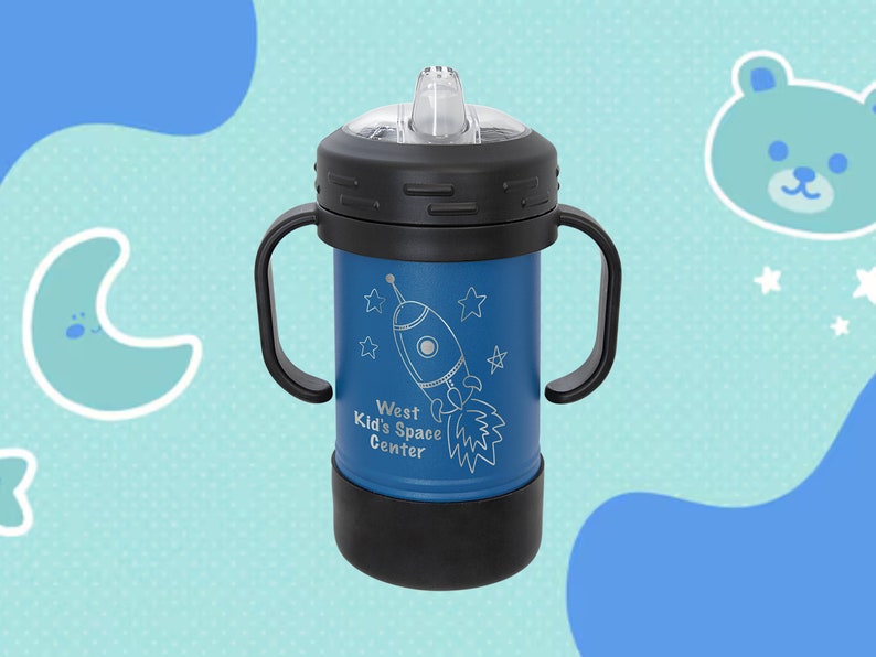Może przedstawiać: Niebieski kubek ze stali nierdzewnej z czarną pokrywką i uchwytami. Kubek ma wz&oacute;r rakiety z tekstem "West Kid's Space Center".