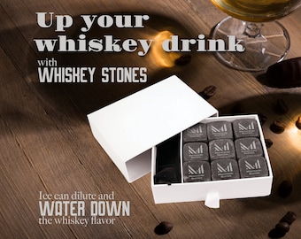 May include: A white box with a drawer containing nine black whiskey stones. The box is open and the drawer is pulled out. The text on the box reads "Whiskey Stones". The text on the stones reads "Mahagiri Stones". The text on the top of the image reads "Up your whiskey drink with WHISKEY STONES. Ice can dilute and WATER DOWN the whiskey flavor."