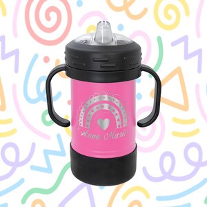 Może przedstawiać: R&oacute;żowy kubek ze stali nierdzewnej z czarną pokrywką i uchwytami. Kubek ma wz&oacute;r tęczy i serca z wygrawerowanym imieniem "Anna Marie".