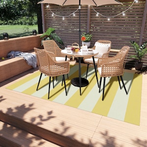 K&ouml;nnte beinhalten: Ein gelber und wei&szlig; gestreifter Outdoor-Teppich mit einem schwarzen Metalltisch und vier Korbst&uuml;hlen. Der Tisch hat eine wei&szlig;e Tischplatte und eine kleine Topfpflanze in der Mitte.