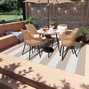 K&ouml;nnte beinhalten: Ein gestreifter Outdoor-Teppich mit einem braunen und wei&szlig;en Muster. Der Teppich liegt auf einem Holzdeck und verf&uuml;gt &uuml;ber einen Tisch und vier St&uuml;hle. Der Tisch ist rund und schwarz mit einer wei&szlig;en Tischplatte. Die St&uuml;hle sind aus Weide und haben schwarze Metallbeine.
