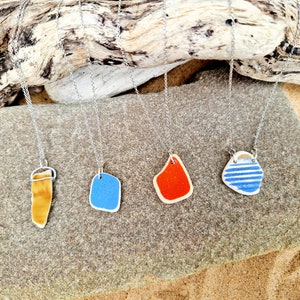 May include: Four necklaces with different sea glass pendants. The pendants are a long, thin, brown piece, a square blue piece, a red piece, and a white piece with blue stripes.