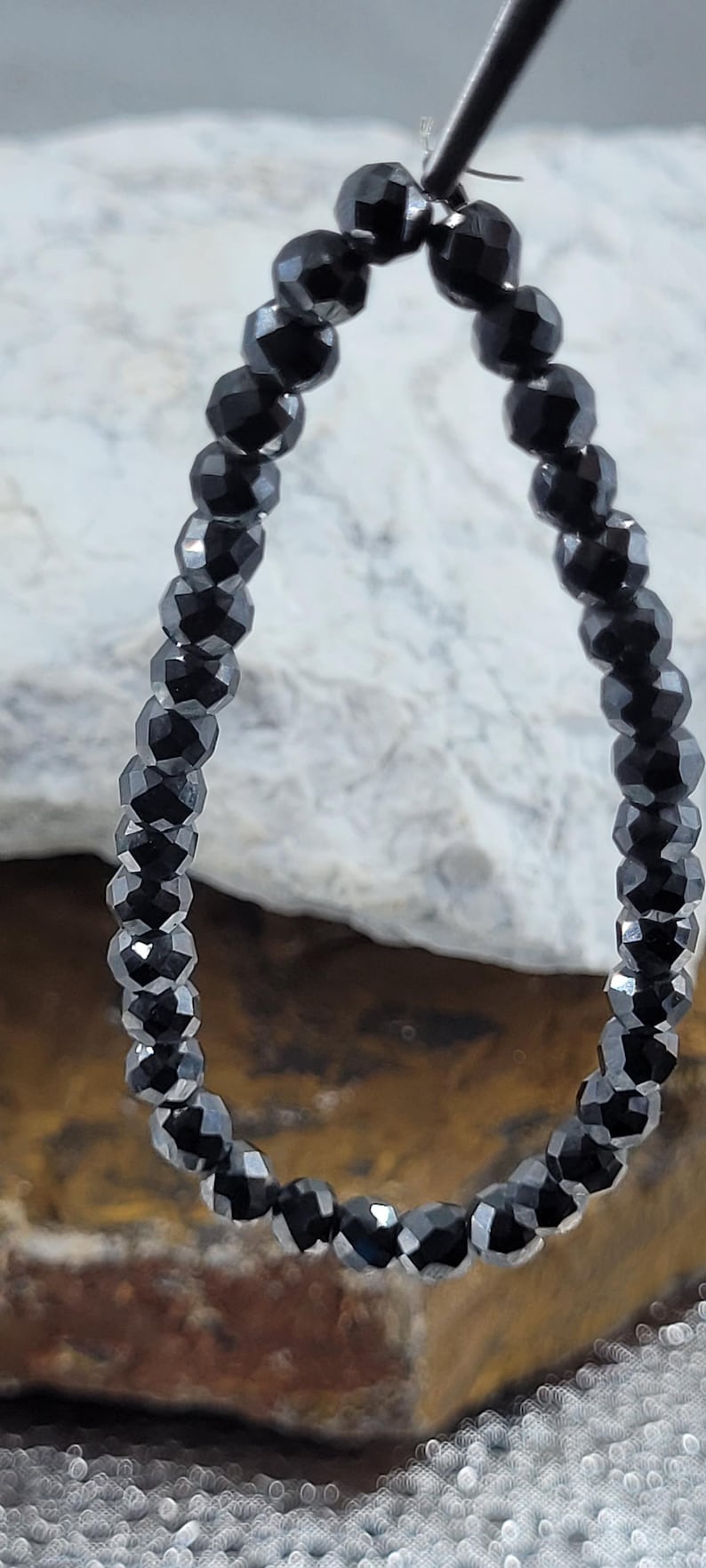 Peut inclure: Un rang de perles noires &agrave; facettes, probablement des pierres pr&eacute;cieuses, enfil&eacute;es ensemble. Les perles sont de taille uniforme et r&eacute;fl&eacute;chissent la lumi&egrave;re, cr&eacute;ant un effet scintillant. L'arri&egrave;re-plan est un m&eacute;lange flou de tons neutres.