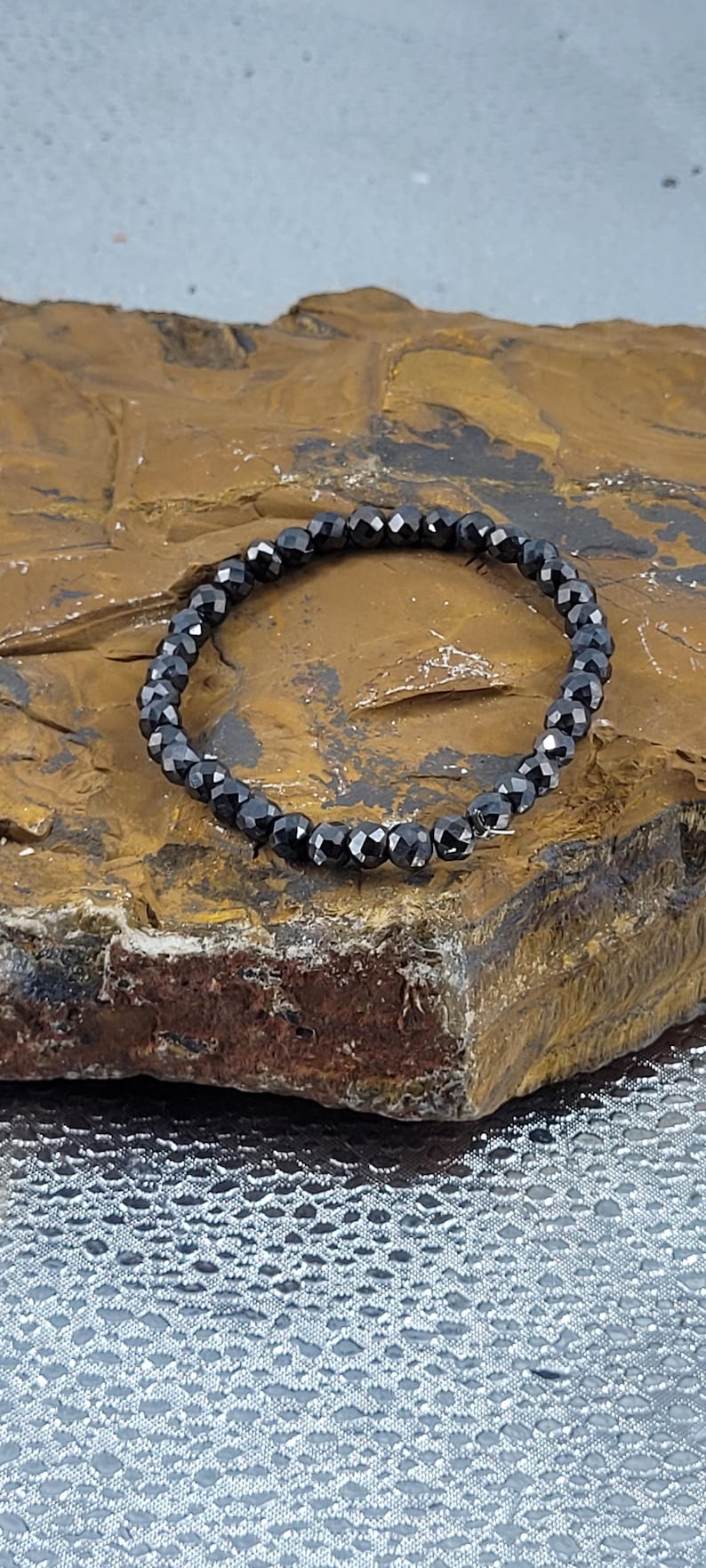 Peut inclure: Un bracelet de perles noires avec des perles &agrave; facettes. Le bracelet est compos&eacute; de petites perles noires rondes enfil&eacute;es ensemble. Le bracelet est pr&eacute;sent&eacute; sur une surface brune textur&eacute;e.