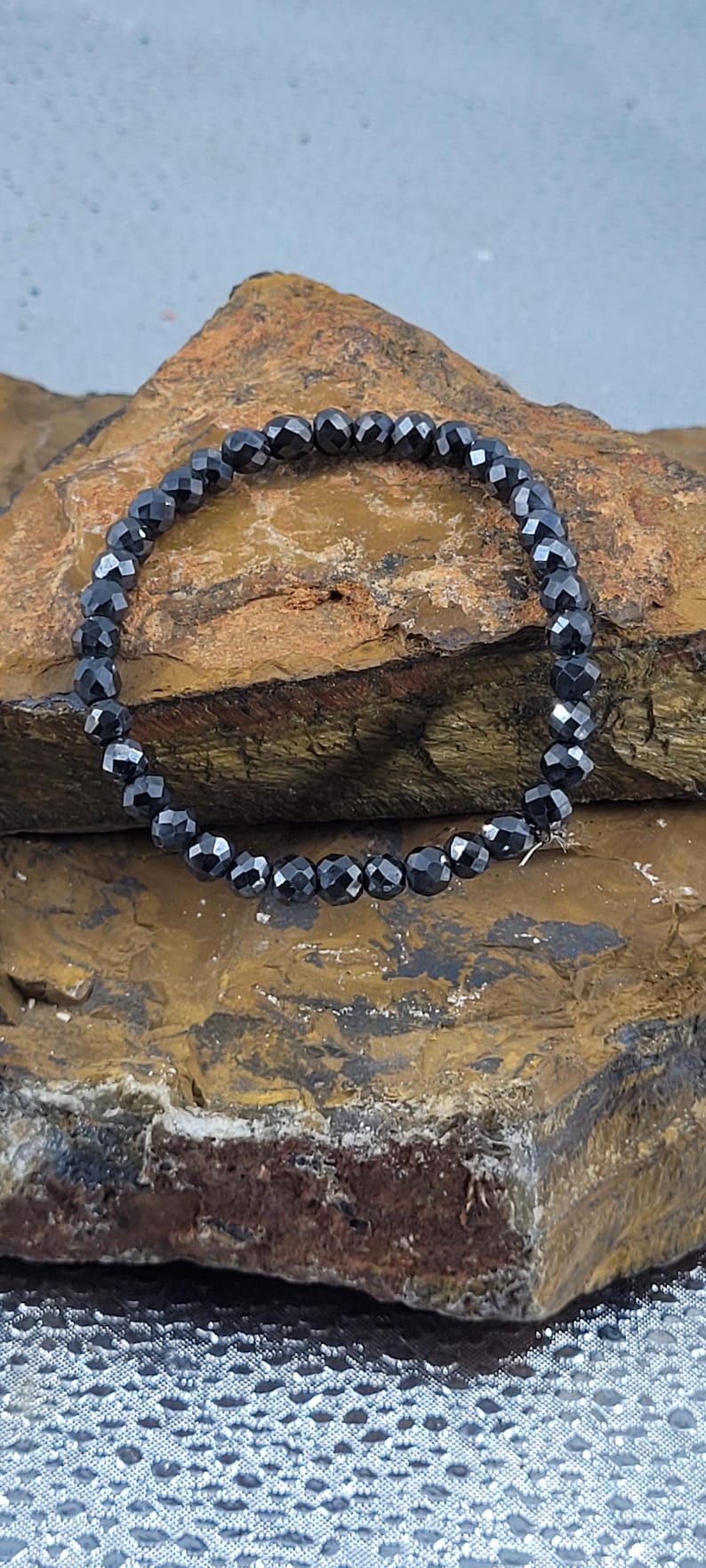Peut inclure: Un bracelet de perles noires avec des perles &agrave; facettes. Le bracelet est mont&eacute; sur un cordon &eacute;lastique et est pr&eacute;sent&eacute; sur une surface brune textur&eacute;e. Les perles ont une qualit&eacute; r&eacute;fl&eacute;chissante.