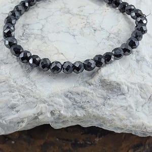 Peut inclure: Un bracelet de perles noires avec des perles &agrave; facettes. Le bracelet est compos&eacute; de petites perles rondes et sombres enfil&eacute;es ensemble. Le bracelet est pr&eacute;sent&eacute; sur une surface claire et textur&eacute;e.