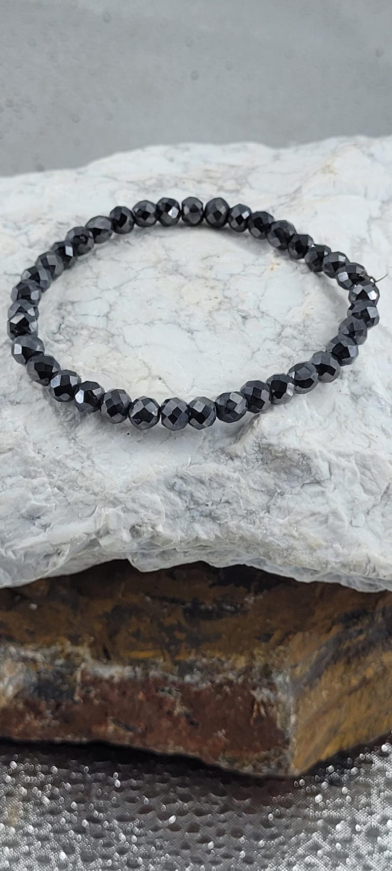 Peut inclure: Un bracelet de perles noires avec des perles &agrave; facettes. Le bracelet est compos&eacute; de petites perles rondes et sombres enfil&eacute;es ensemble. Le bracelet est pr&eacute;sent&eacute; sur une surface claire et textur&eacute;e.