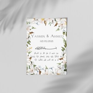 以下が含まれることがあります： 「YASMIN & AHMED」と日付「02/05/2021」が記載された長方形の結婚式の招待状。白い花と緑の葉のアクセントでデザインされています。アラビア語のテキストも含まれています。