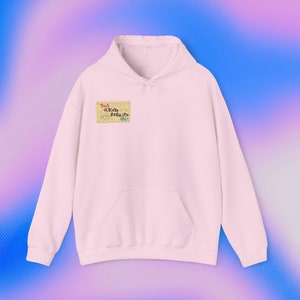 Op de afbeelding: Een lichtroze hoodie met een kangoeroezak en een capuchon met trekkoord. De hoodie heeft een kleine rechthoekige afbeelding op de borst met Japanse tekst en cartoon illustraties. De stijl is casual en comfortabel.