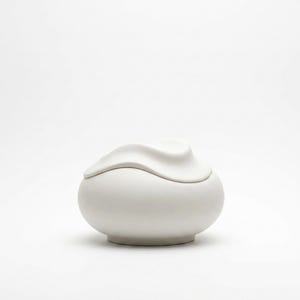 Pode incluir: Um pote de cer&acirc;mica branco com tampa. O pote tem uma base arredondada e uma tampa com uma forma ondulada e org&acirc;nica. O pote &eacute; de cor branca mate s&oacute;lida e assenta sobre um fundo branco.