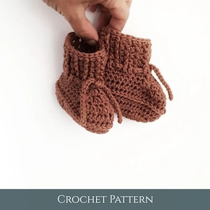 May include: A pair of handmade, brown crochet baby booties. The booties have a ribbed cuff and a laced closure. The text "CROCHET PATTERN" is at the bottom of the image.