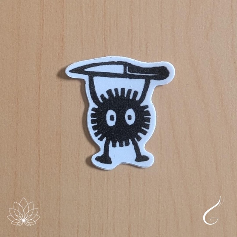 May include: A die-cut sticker featuring a black and white graphic illustration of a round, spiky creature with two eyes, two legs, and arms raised above its head while holding a long, horizontal knife across the top of its body.