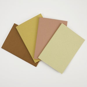 May include: Four small notebooks with different colored covers: brown, yellow, pink, and light green. The notebooks are arranged in a fan shape.