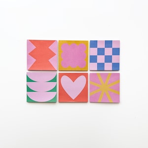 Op de afbeelding: Zes kleurrijke vierkante plakbriefjes met verschillende geometrische patronen. De briefjes zijn roze, oranje, groen, geel en blauw.