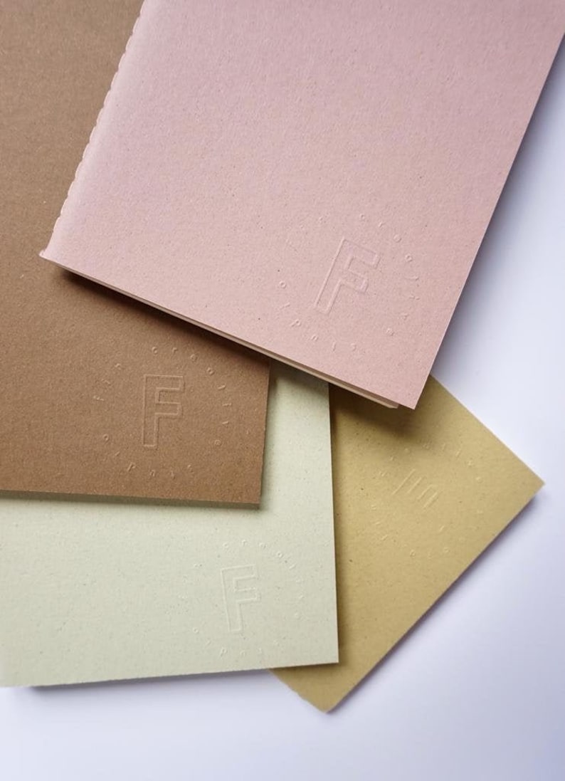May include: Four sheets of paper in different colors, brown, beige, light green, and pink, are stacked on top of each other. Each sheet has a circular embossed logo with the letter "F" in the center.