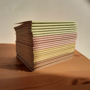 May include: A stack of notebooks with light green and pink covers. The covers have a dotted pattern and are stitched together.