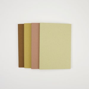May include: Four notebooks stacked together, each with a different color cover: brown, yellow, pink, and light green.