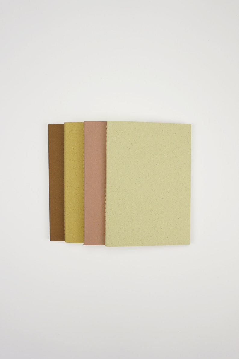 May include: Four notebooks stacked together, each with a different color cover: brown, yellow, pink, and light green.