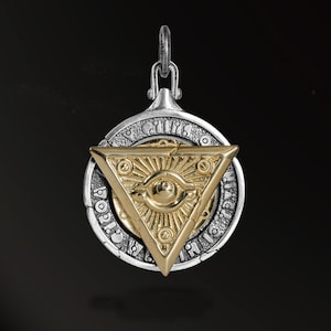 May include: A silver pendant with a gold-colored triangle featuring an eye design at the center. The pendant has a circular frame with engraved details and a small loop for a chain. The design is set against a dark background.