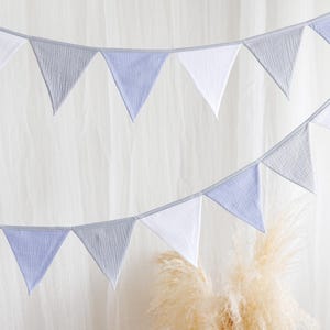 May include: A decorative banner with triangular flags in white, light blue, and gray. The flags are strung on a gray cord, creating a festive and charming aesthetic. The banner is suitable for various celebrations and events.