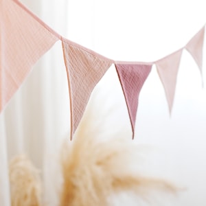 May include: A pink and white fabric bunting with triangular flags hanging from a white background.