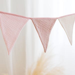 May include: A pink and white fabric bunting with triangular flags. The flags are made of a soft, gauzy material and are strung together with a white cord.