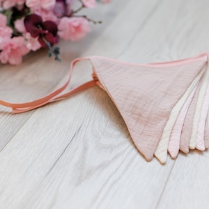 May include: A pink and white fabric bunting with a pink ribbon. The bunting is made of soft, lightweight fabric and is perfect for adding a touch of whimsy to any party or event.