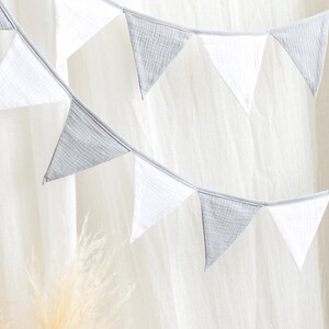 May include: A decorative banner with alternating white and gray triangular flags. The flags are strung together on a thin, light-colored string. The banner is set against a soft, white background.