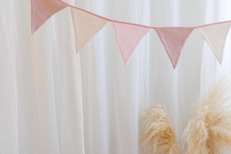 May include: A pink and cream fabric bunting with triangular flags hanging against a white background.