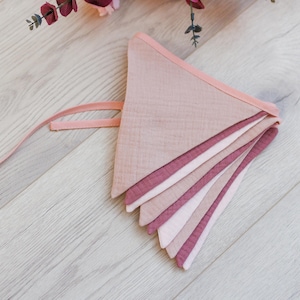 May include: A pink and white fabric bunting with a pink ribbon attached. The bunting is made of multiple layers of fabric, creating a layered effect.