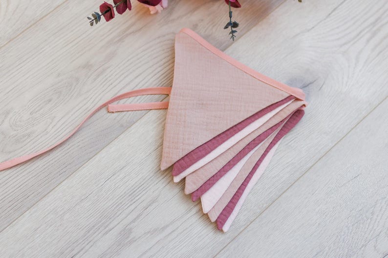 May include: A pink and white fabric bunting with a pink ribbon attached. The bunting is made of multiple layers of fabric, creating a layered effect.