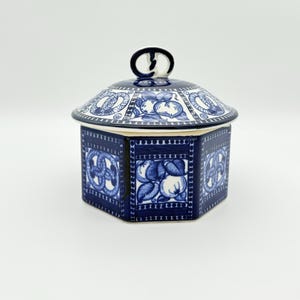 Peut inclure: Un pot hexagonal en céramique bleu et blanc avec un couvercle. Le pot présente un motif floral et de nœuds répété. Le couvercle a une poignée en boucle et un motif floral. Le pot est probablement à des fins décoratives ou de stockage.