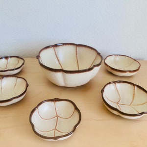 Könnte beinhalten: Ein Set aus sechs Keramikschalen mit Blattmuster. Die Schalen sind cremefarben mit braunen Rändern und Blattaderdetails. Das Set enthält eine große Schale und fünf kleinere Schalen, alle mit einem gewellten Rand.