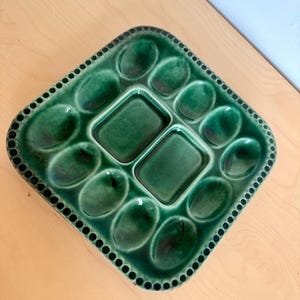 May include: A vintage, emerald green ceramic oyster serving platter. The platter has a diamond shape with oval indentations for oysters and two rectangular wells. A dotted border frames the edges.