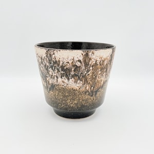 May include: A ceramic planter with a unique, textured glaze. The planter features a dark brown rim and base, with a blend of white, brown, and gold tones in the middle. The planter has a wide opening and a slightly flared shape.