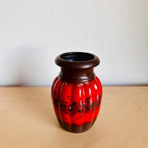 May include: A small, vintage ceramic vase with a ribbed design. The vase features a vibrant red glaze with dark brown speckles and a dark brown rim and base. The interior is dark. A decorative piece for home decor.