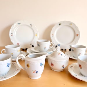 Può includere: Servizio da tè in porcellana bianca con un motivo floreale. Il set comprende tazze, piattini, piatti, una lattiera e una zuccheriera. Ogni pezzo è decorato con fiori colorati e ha un bordo smerlato.