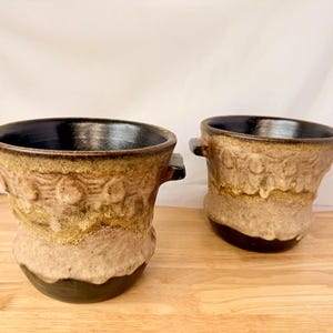 May include: A white ceramic mug with a black handle and the text "But First, Coffee" in a black, handwritten-style font. The mug sits on a white surface.