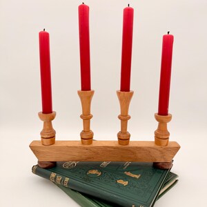 May include: A wooden candelabra with four turned pillars holding four tall red taper candles, resting on two stacked green hardcover books with gold embossed lettering and decorative illustrations on the front covers.